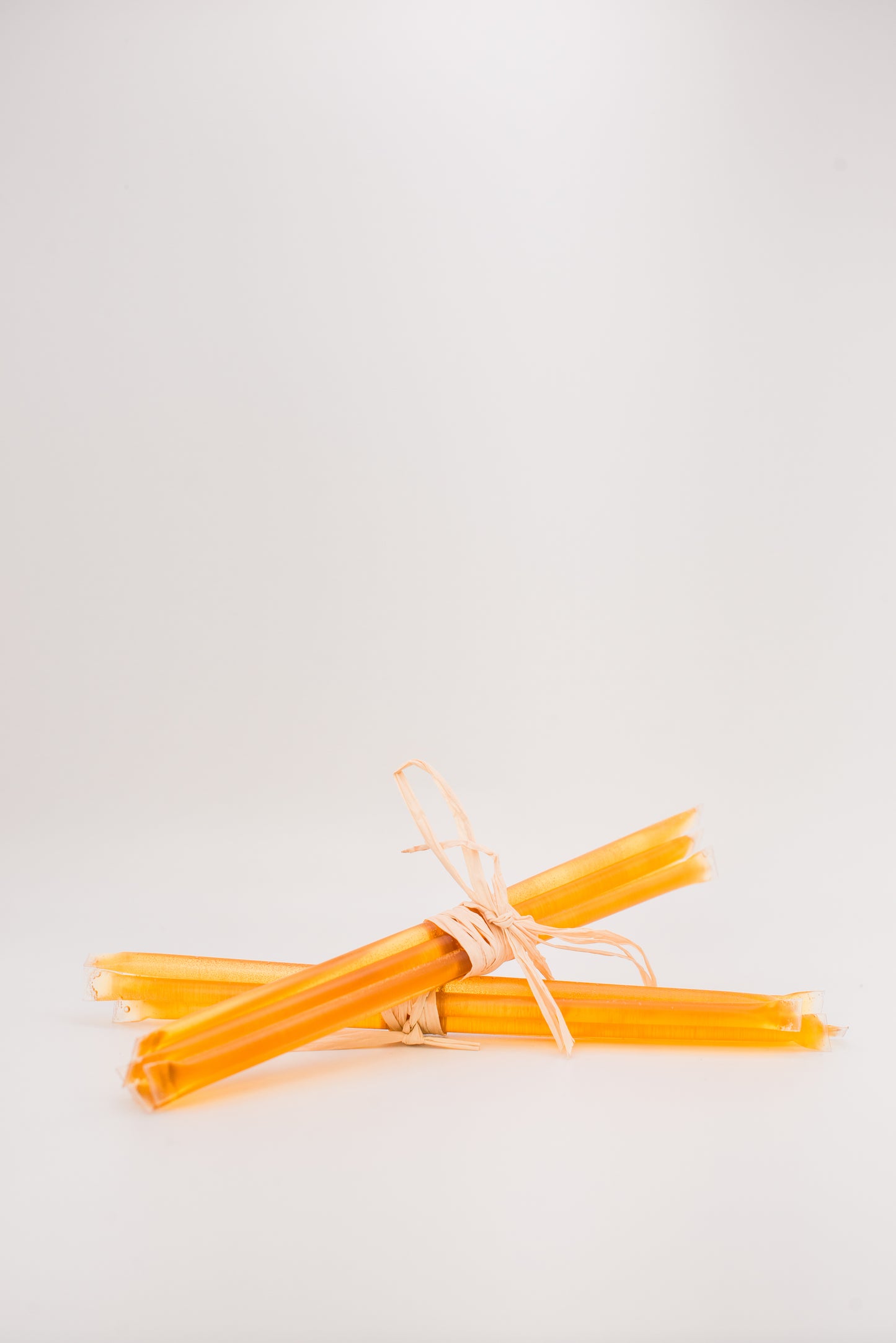 A bundle of thin, yellow Honey Straws by Honeybee tied together with natural twine, reminiscent of wildflower honey, placed against a plain white background. The Honey Straws are arranged in a simple, rustic style.