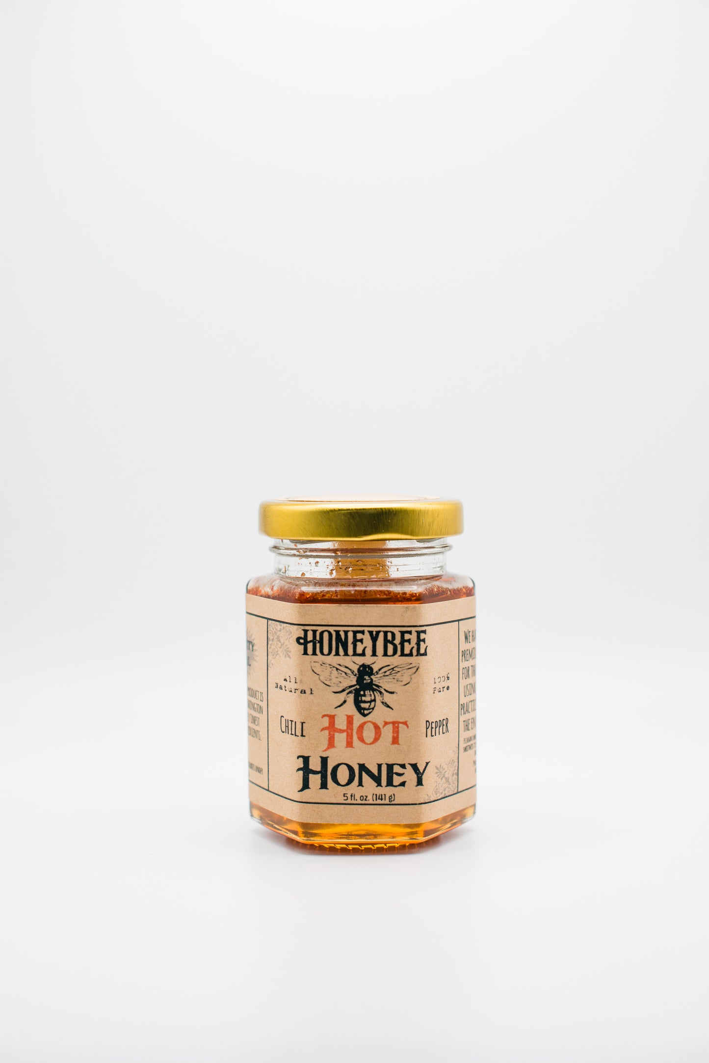 A jar of Honeybee's 'Hot Honey' with a gold lid set against a plain white background. The label features an illustration of a bee and emphasizes that the raw wildflower honey is infused with hot chili peppers, suggesting a spicy flavor.