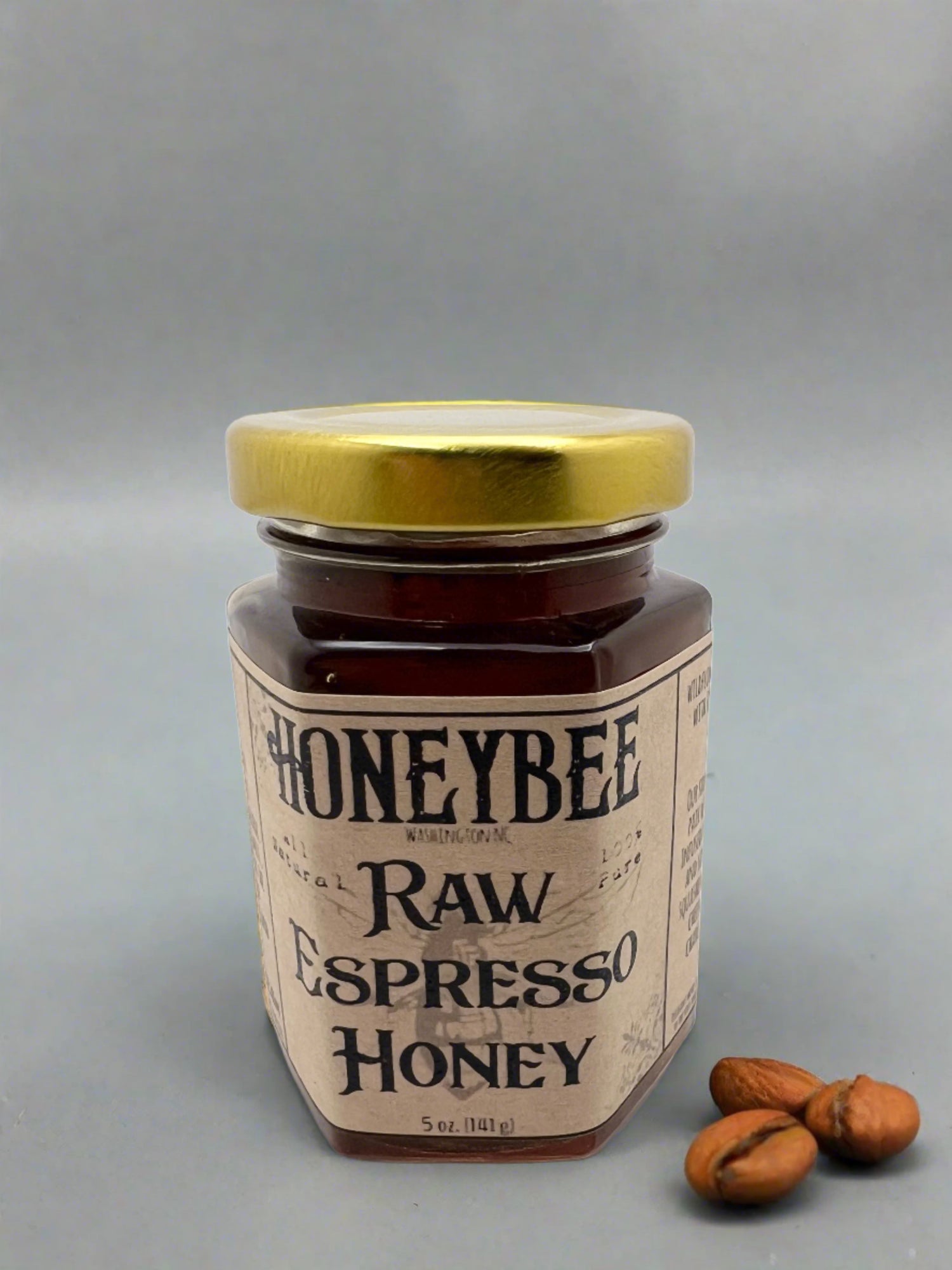 A jar of Honeybee Espresso Honey with a gold lid and a few nuts.